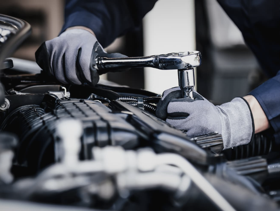 Expert performing car repair services with a wrench on an engine under the hood.