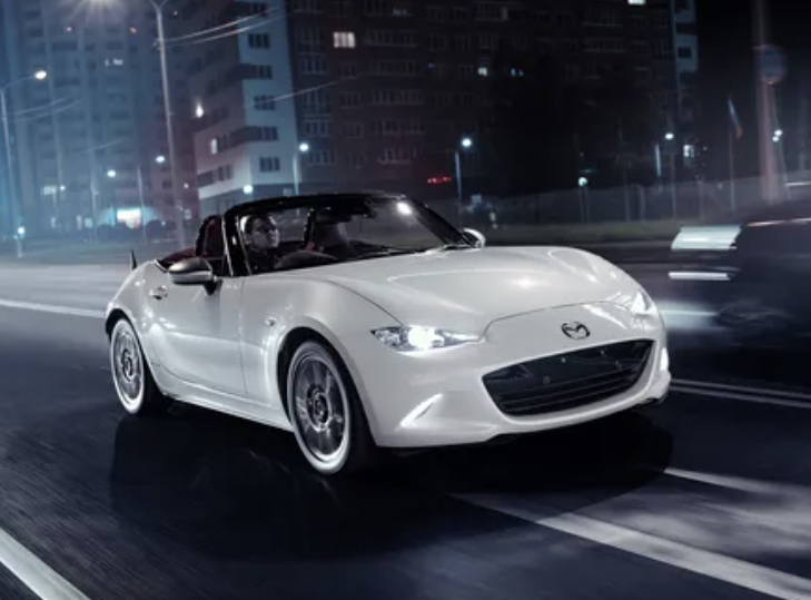 Mazda MX5 car parts showcased with a sleek white sports car driving at night on a city street.