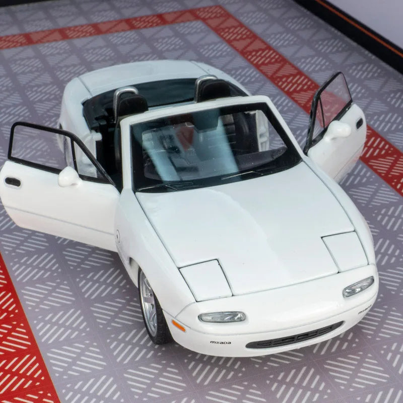 Mazda MX5 die cast toy car model in white color with open doors on a garage-themed background.