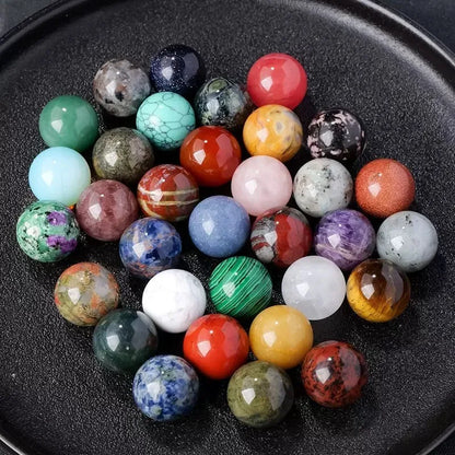 Natural crystal ball beads in various colors and sizes displayed on a black plate, ideal for DIY jewelry crafts.